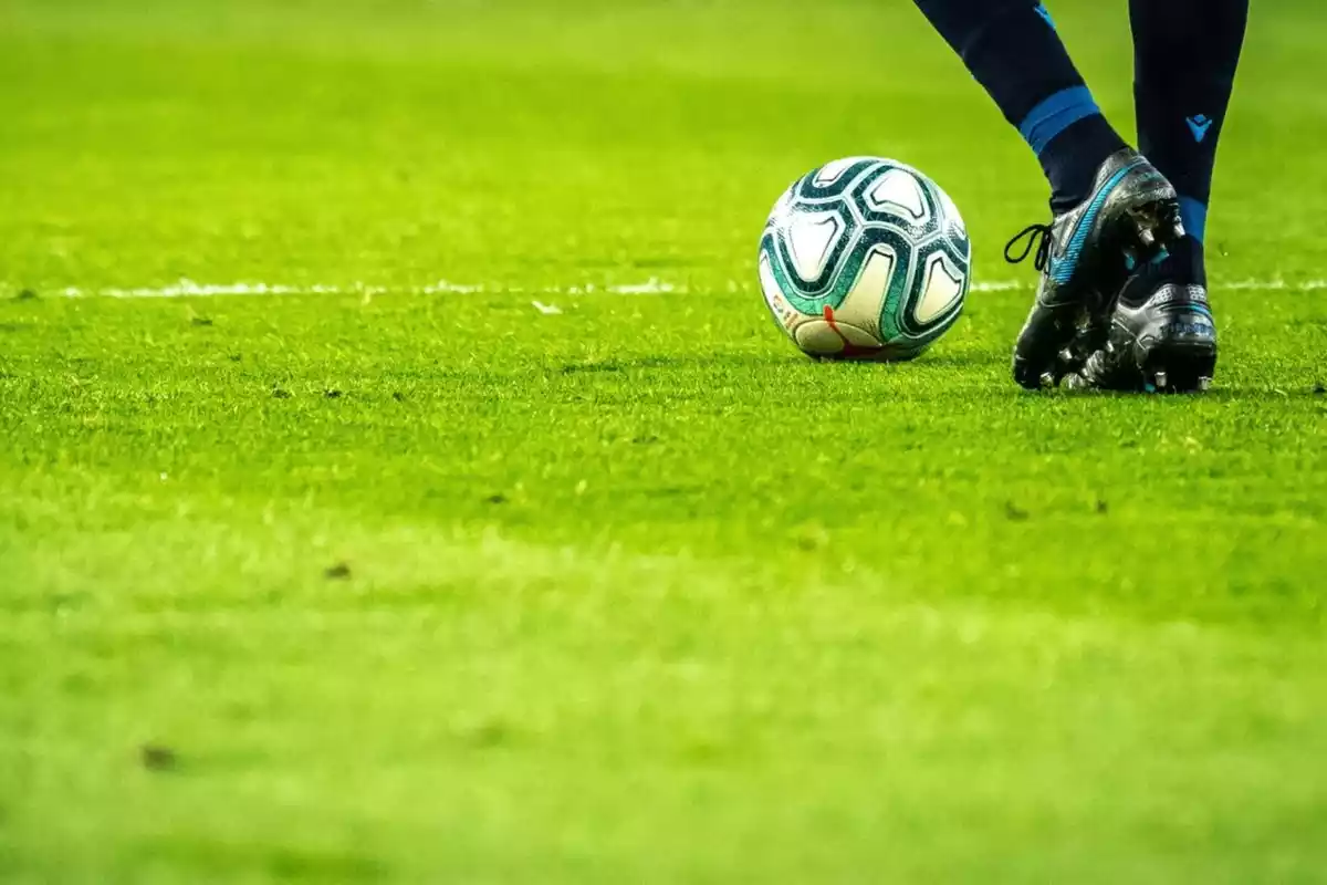 campo de futobl de céspedo con unos pies y una pelota