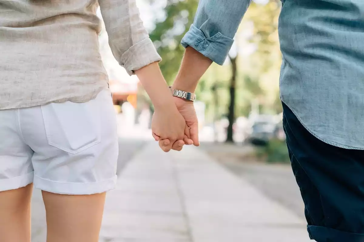 Una pareja cogida de la mano paseando por las calles de su localidad en un día de sol