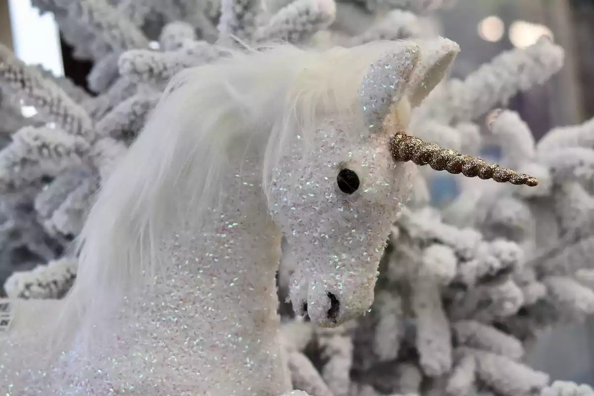 Un unicornio blanco de peluche delante de un árbol de navidad