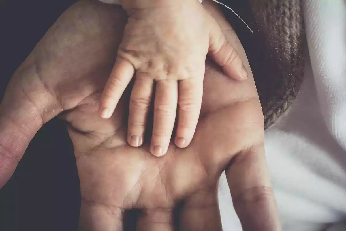 Una mano de padre con la mano de su hijo encima