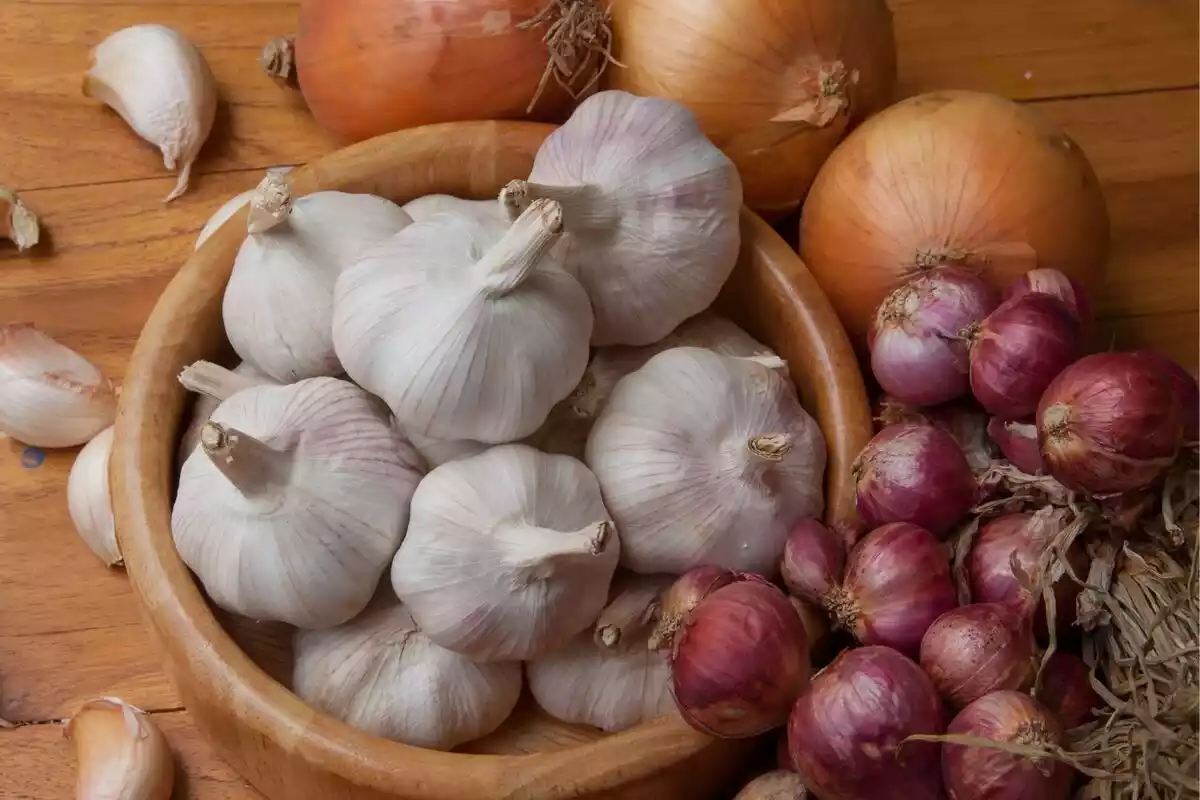 Ajos blancos y cebollas rojas y naranjas en una mesa de madera