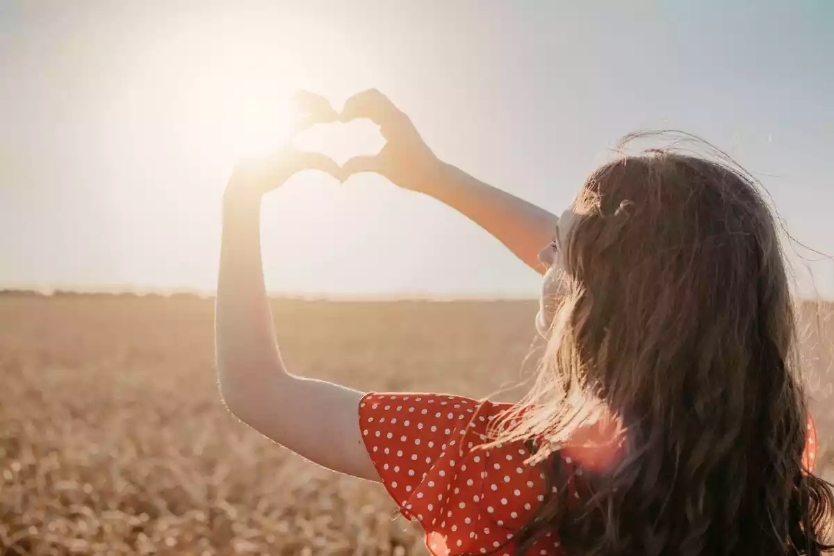 Una mujer con vestido rojo haciendo un corazón con las manos levantadas bajo el sol