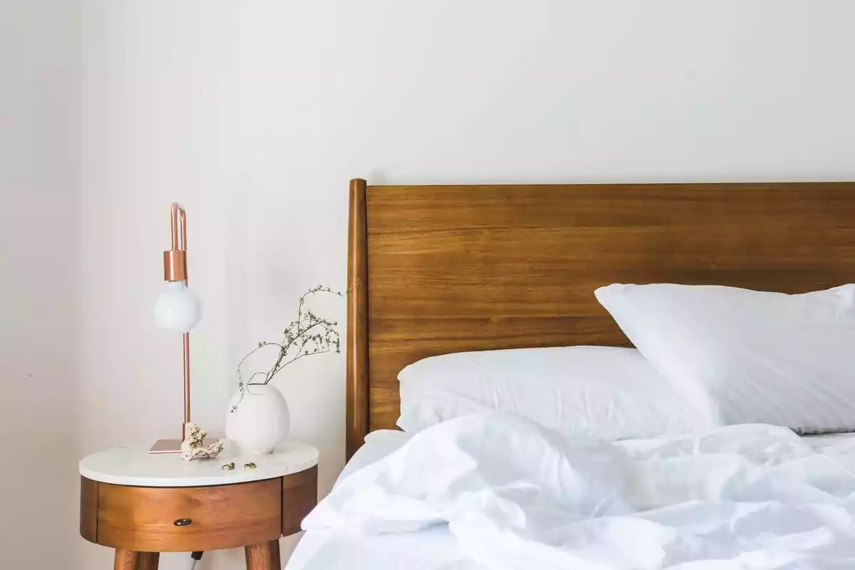 Cama con cabecera de madera y una mesa de noche con una lámpara