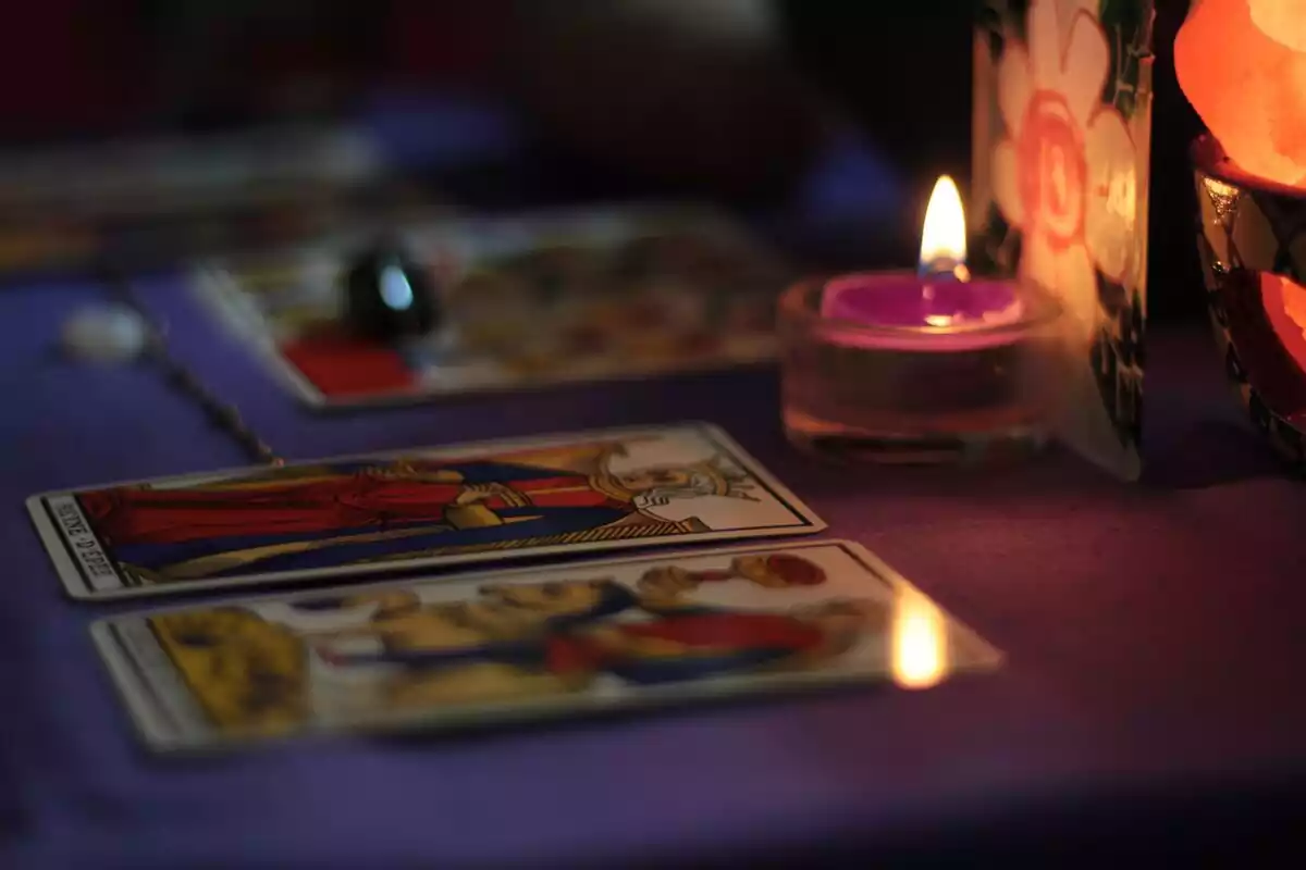 Dos cartas de tarot sobre una mesa junto a una vela encendida