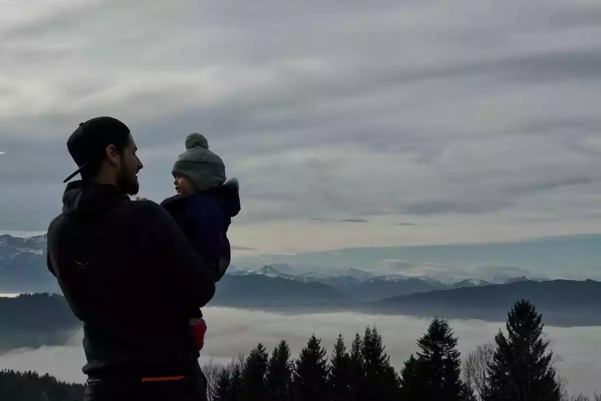 Hombre con un bebé en brazos y de fondo montañas y árboles