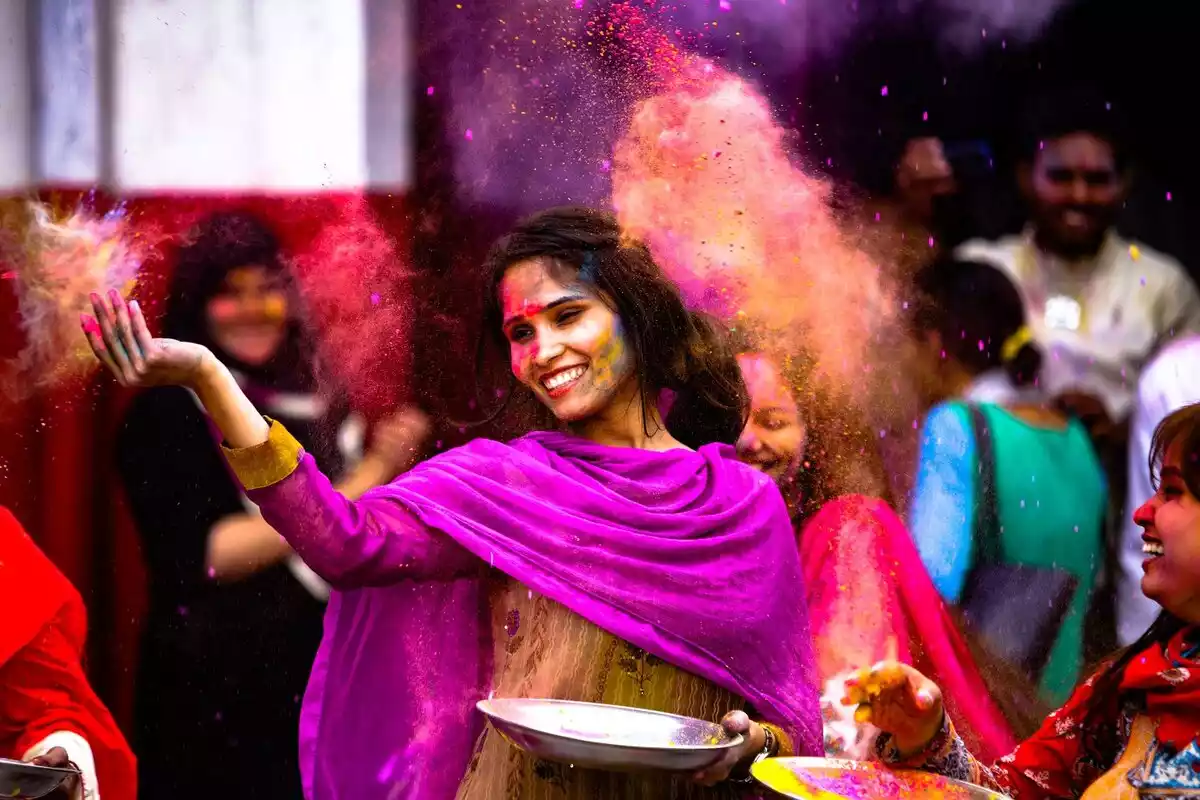 Mujer hindú sonriendo y esparciendo polvos de colores