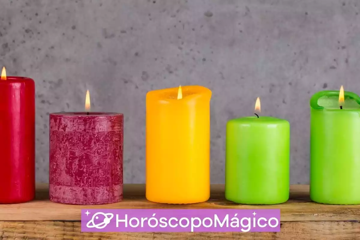 5 velas de colores encendidas sobre una mesa de madera y un fondo gris