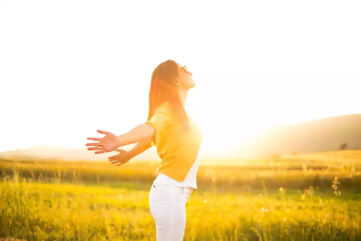 Imagen lateral de una mujer con los brazos hacia atrás y una puesta de Sol de fondo