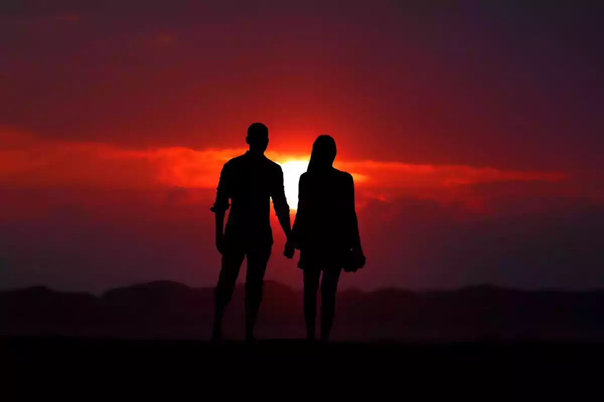 Pareja agarrada de la mano frente al atardecer