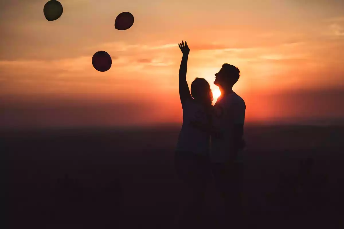 Pareja frente al atardecer tirando globos