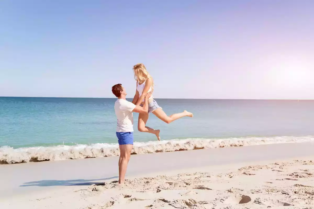 Un chico sostiene en el aire a una chica frente al mar