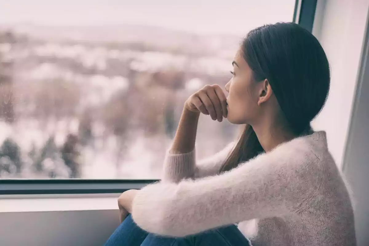 Chica morena mira un paisaje por la ventana nevado