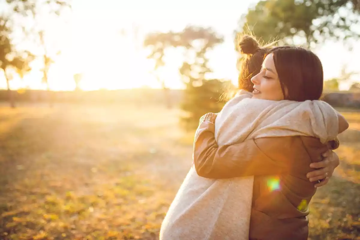 Dos chicas se abrazan en un bosque con la puesta de sol