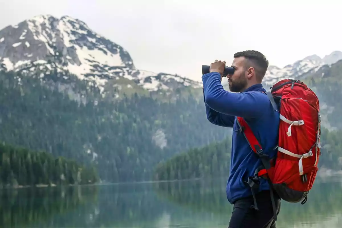 Hombre mirando por unos prismáticos con un lago y una montaña al lado