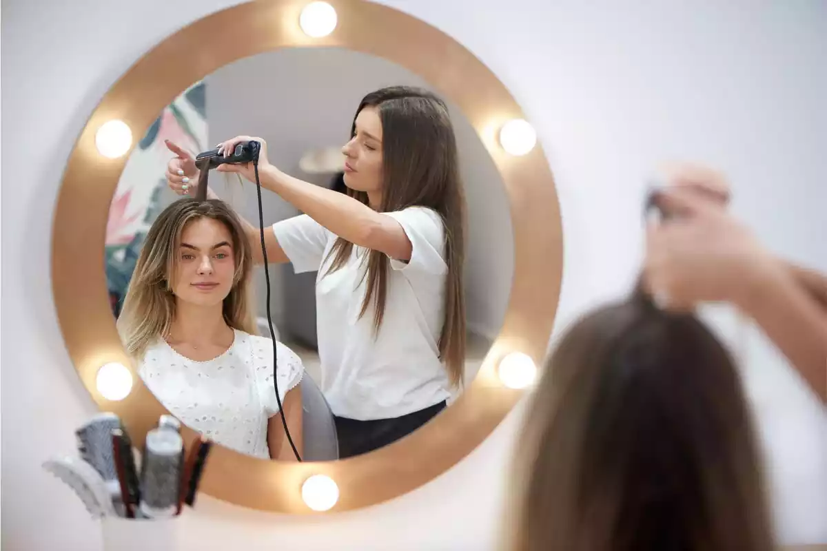 Reflejo de una mujer peinando el cabello de otra en un espejo marrón con luces