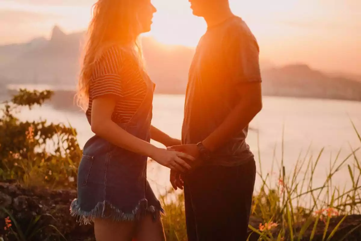 Una chico y una chica agarrados de la mano con una puesta de Sol de fondo