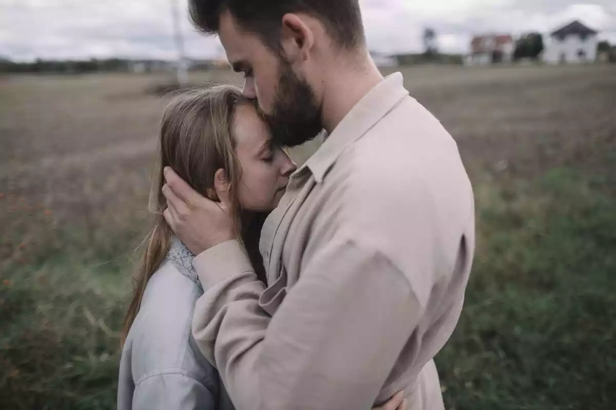 Una pareja en un campo, el hombre le da un beso en la frente