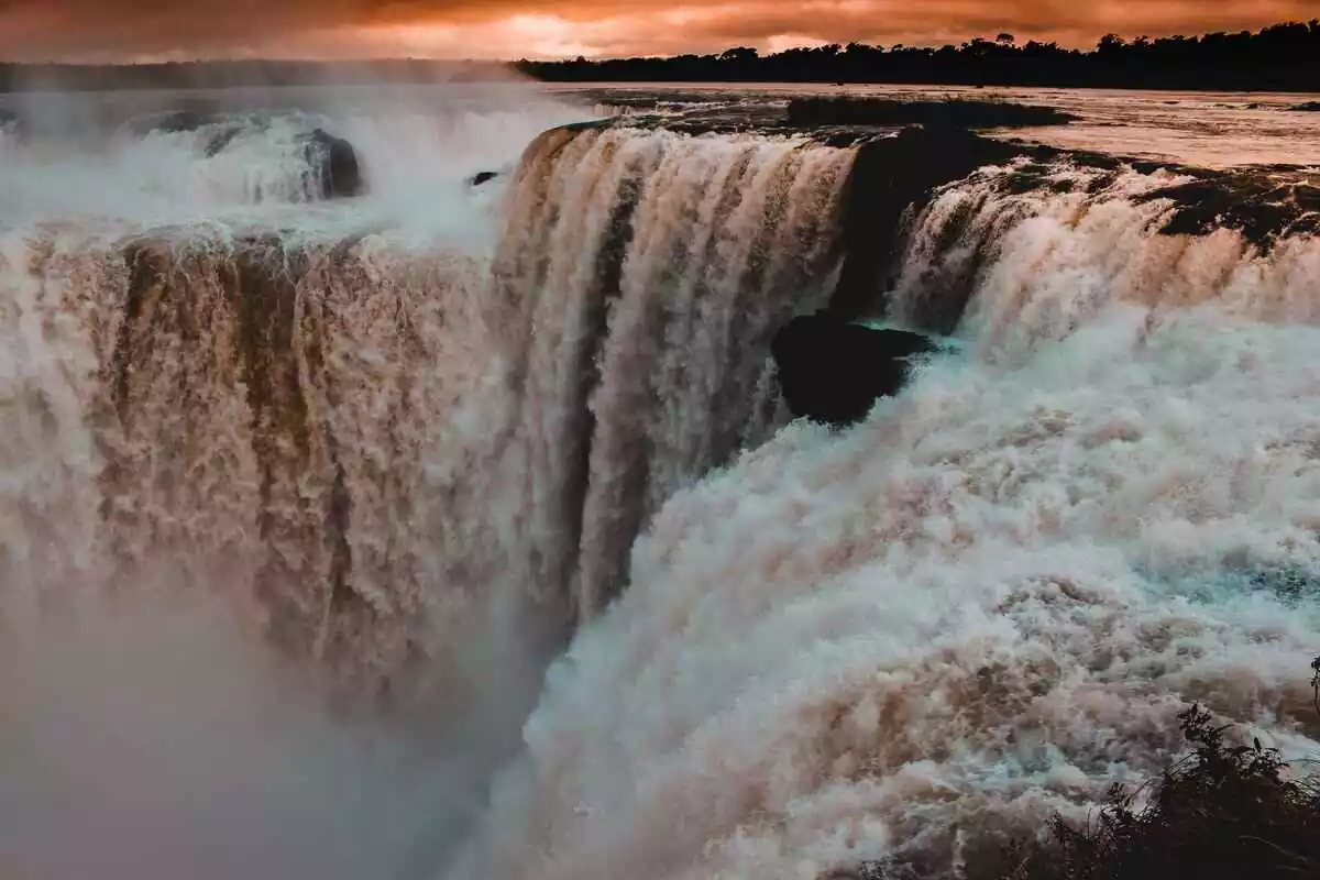 Imagen de una cascada con un atardecer de fondo