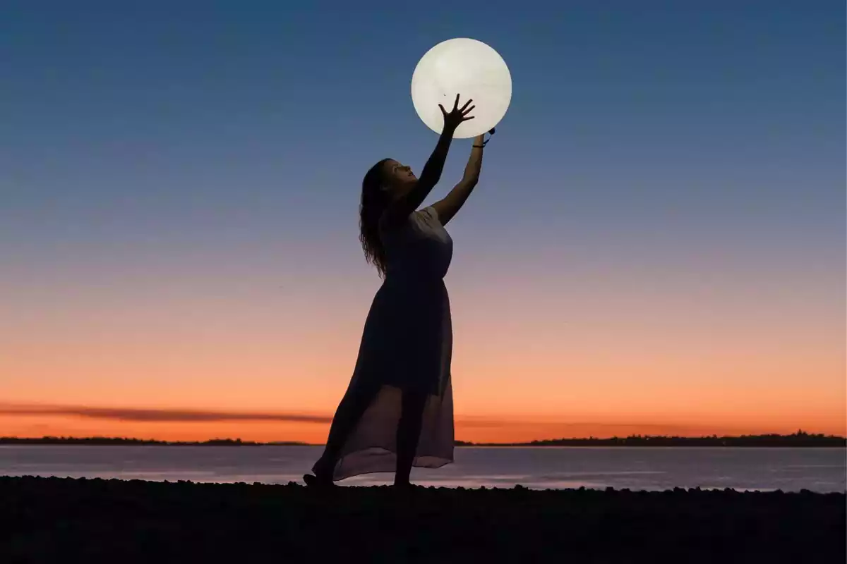 Una chica en el mar sujetando una lámpara en forma de luna