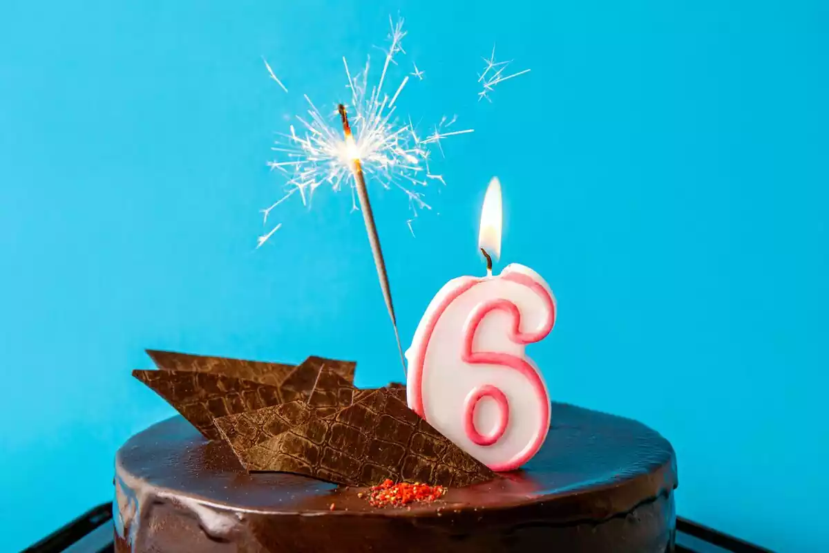 El número 6 encima de una tarta de cumpleaños con una bengala y unos barquitos de chocolate