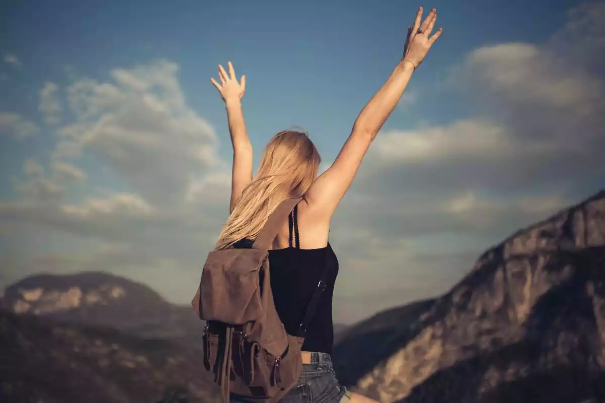 Una chica feliz con los brazos bien estirados hacia arriba gritando delante de un paisaje