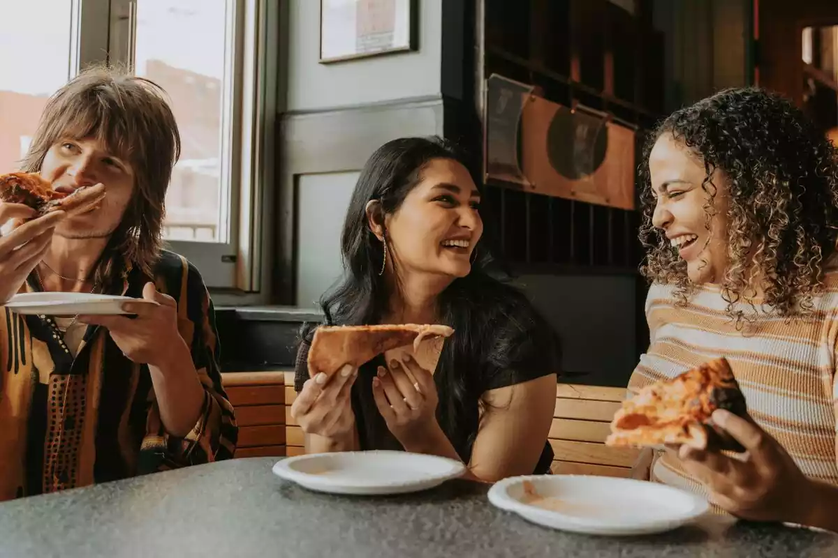 Tres personas comiendo pizza en un restaurante